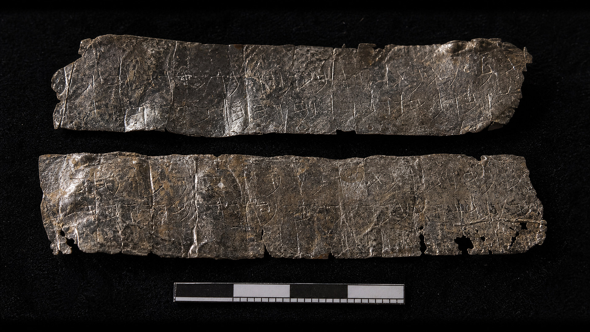 Deux fines feuilles d'argent déroulées, couvertes de lettres gravées, avec une échelle de mesure