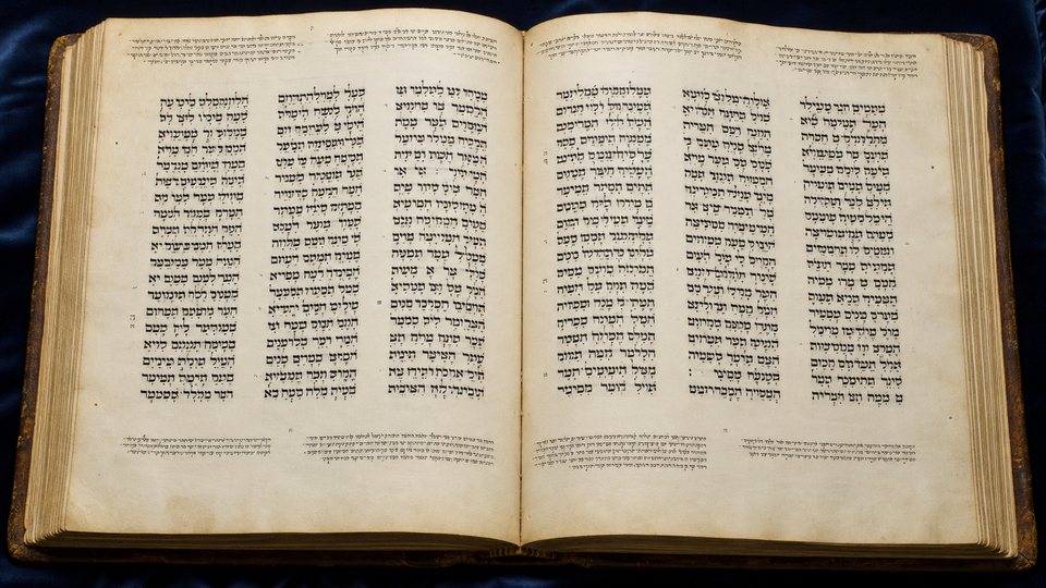 Un grand codex hébreu ouvert sur du velours bleu, chaque page écrite en trois colonnes
