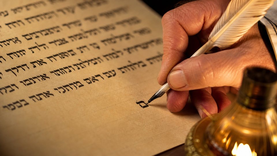 Gros plan sur la main d'un scribe traçant une lettre hébraïque à la plume sur un parchemin